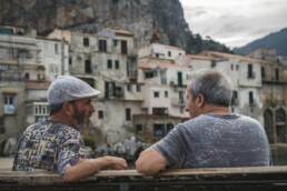 two middle aged men sitting on a bench together and discussing financial challenges