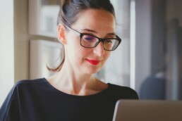 a woman wearing glasses, looking at a tablet screen and reviewing her low-interest investments