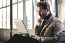 A man sitting in front of a window with a laptop on his lap, following smart money psychology practices and studying his finances