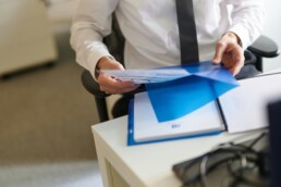 a beginner investor in a button-down shirt and tie, sitting at a desk and reviewing his financial reports stored in a blue plastic folder