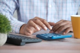 A man's hands operating a blue calculator atop a wooden surface, calculating his separately managed accounts