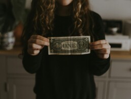 A young girl in a black hoodie demonstrating her financial literacy by displaying a dollar bill from her allowance.
