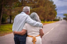 A behind view of a retired senior couple standing on an empty road embracing