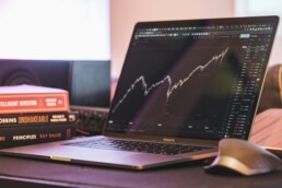 A laptop sitting on a desk beside a stack of investment books. The screen shows a chart that measures changes in market cycles for a particular investment.