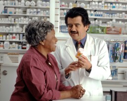 An elderly woman with health insurance speaking with her pharmacist about a new prescription.