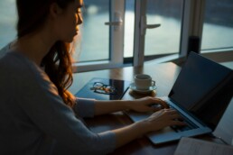 A young woman using a laptop at a desk, practicing ways to avoid online scams