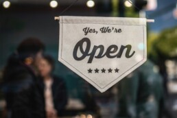 A small business storefront displaying a sign saying the establishment is open for business.
