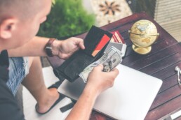 A man sitting at a table and counting his bills to prevent invisible expenses from impacting his budget.